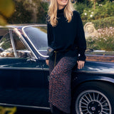 Woman standing next to a vintage car with autumn foliage in the background