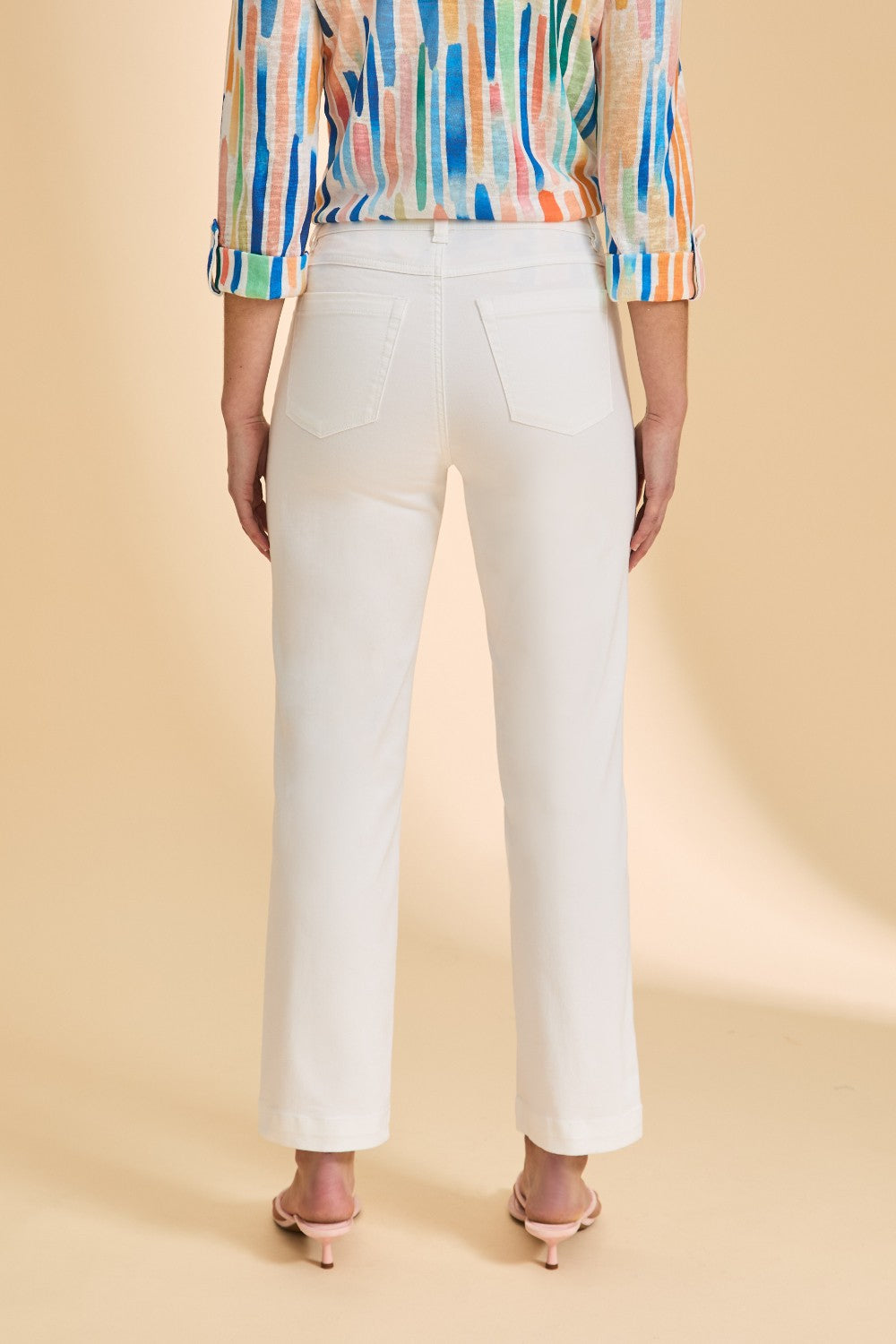 Person wearing a colorful shirt and white pants on a beige background