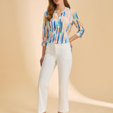 Woman wearing a colorful blouse and white pants on a beige background