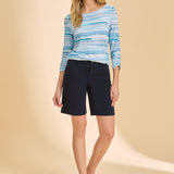 Woman wearing a blue striped sweater and navy shorts on a beige background