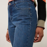 Close-up of a person wearing medium-wash blue jeans with a subtle diamond argyle knit pattern on the front, paired with a pink and black color-blocked sweater.
