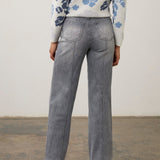 Woman wearing a gray wide leg jean with a printed top and pumps on a neutral background.