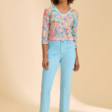 Woman wearing blue ankle pant paired with patterned top against beige background