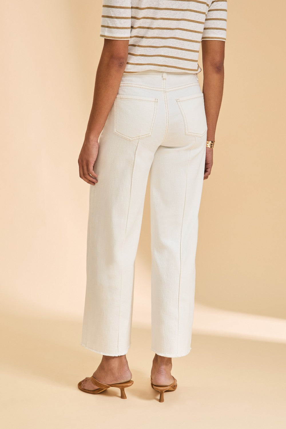 Person wearing ivory pants and a striped shirt on a beige background