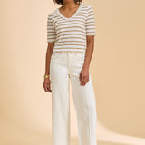 Woman wearing a striped shirt and ivory pants on a beige background