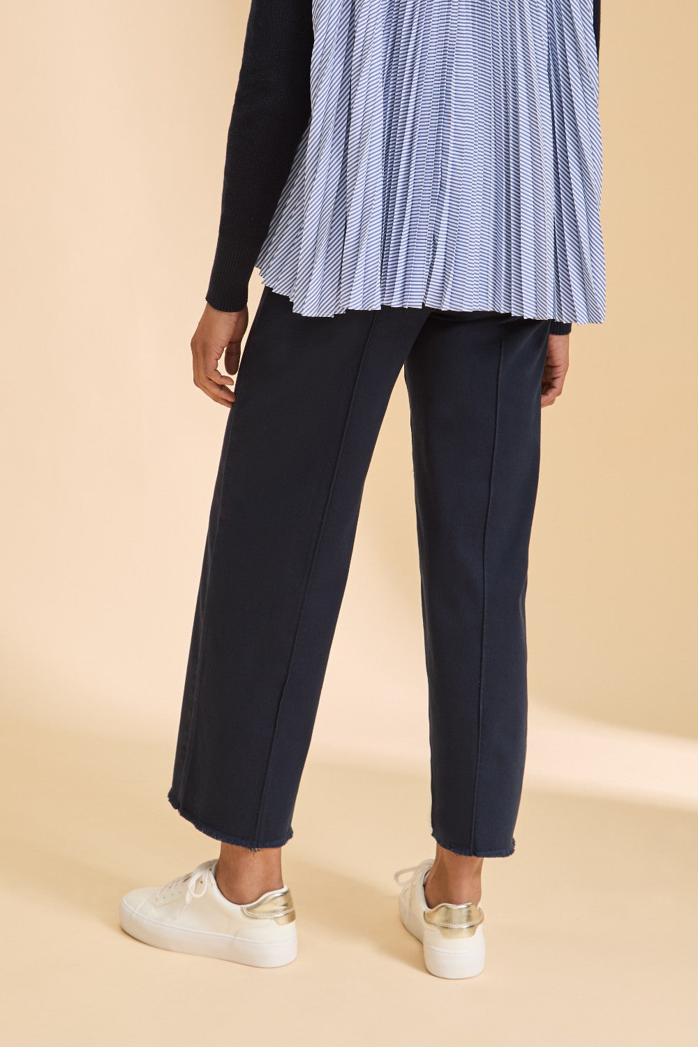 Person wearing navy pants and a blue checkered top on a beige background