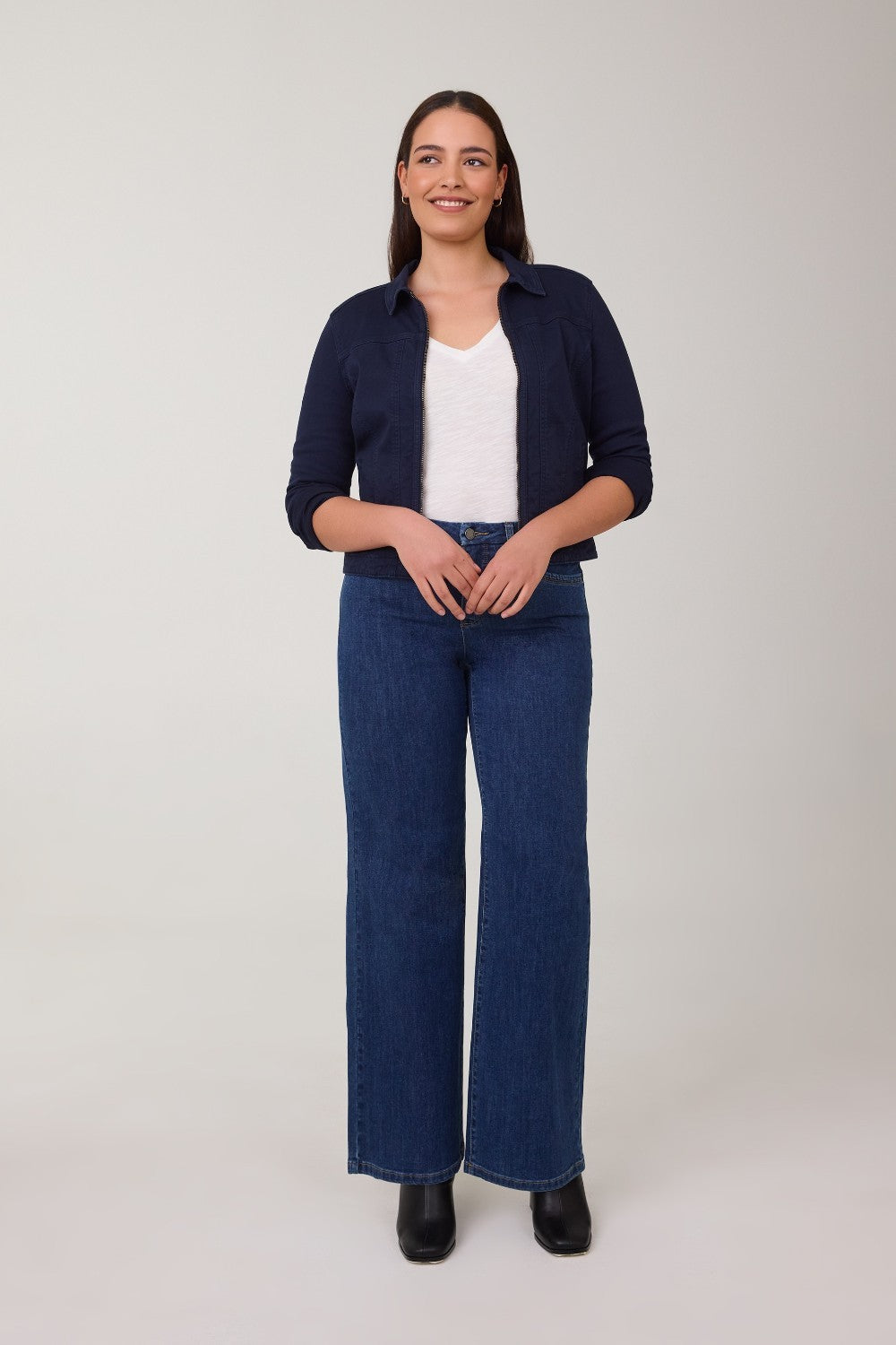 Woman wearing a navy cardigan, white shirt, and blue jeans on a plain background