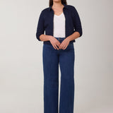 Woman wearing a navy cardigan, white shirt, and blue jeans on a plain background