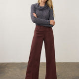 Woman wearing a wide leg pant with a patterned top and pumps on a neutral background.