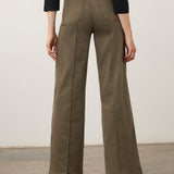Person wearing a green wide leg pant with a black top and black shoes on a neutral background.
