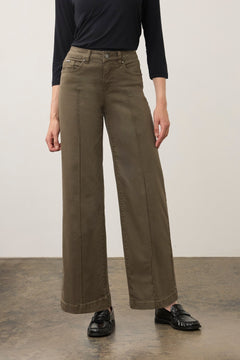 Person wearing a green wide leg pant with a black top and black shoes on a neutral background.