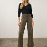 Woman wearing a green wide leg pant with a black top and black shoes on a neutral background.