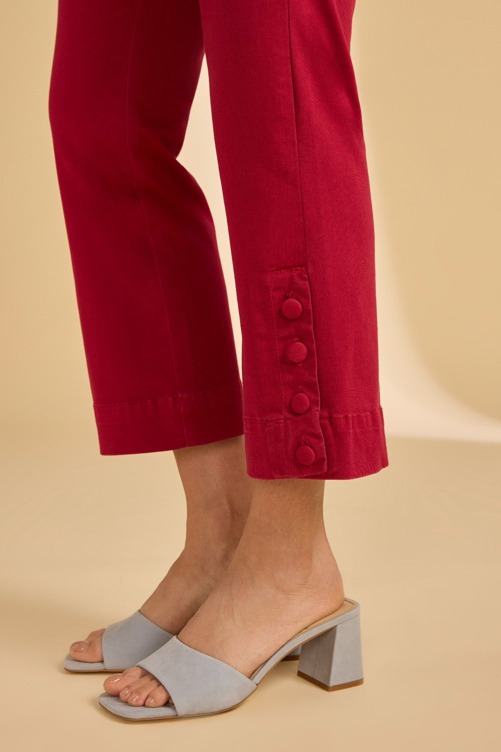 Person wearing red pants with button details and gray open-toe shoes on a beige background