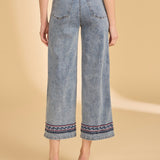 Person wearing blue jeans with decorative hem on a beige background