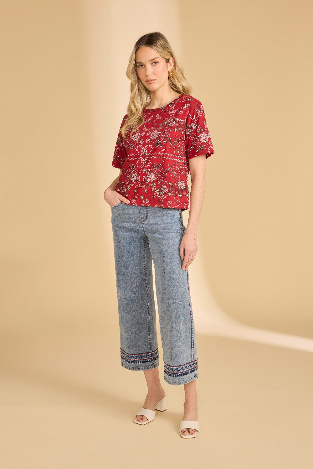 Woman wearing a red patterned top and blue jeans on a beige background