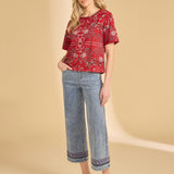 Woman wearing a red patterned top and blue jeans on a beige background