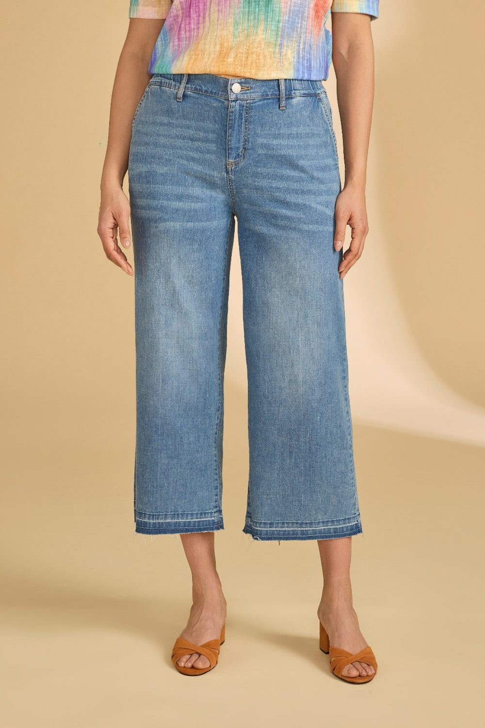 Person wearing blue jeans and a colorful top on a beige background