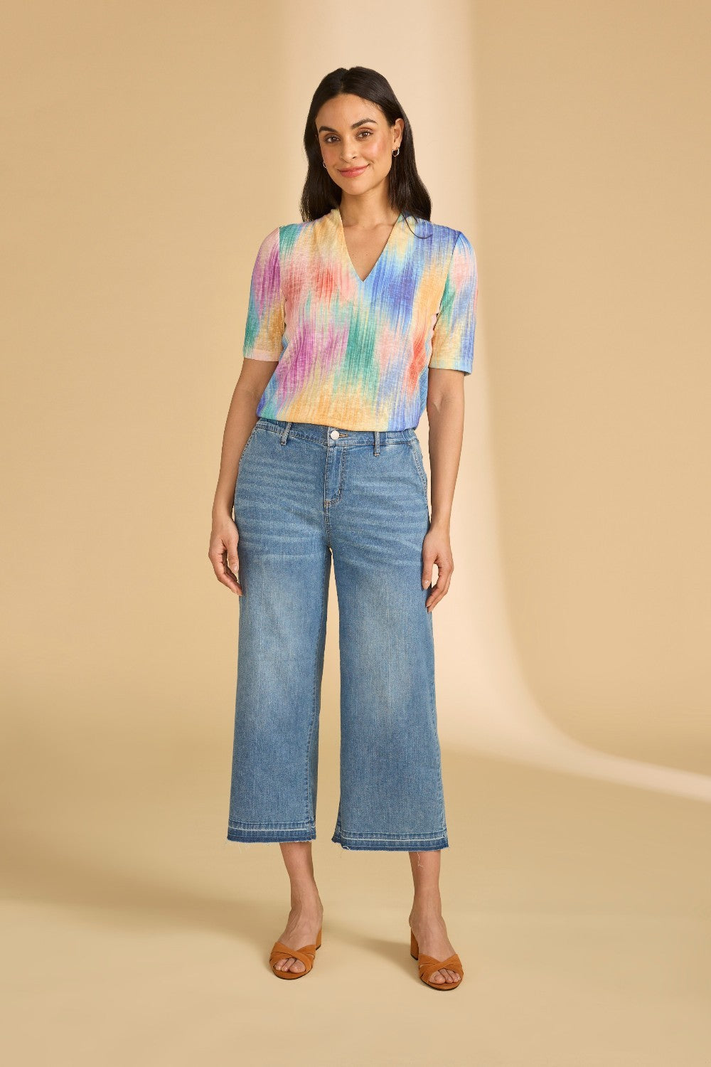 Woman wearing a colorful shirt and blue jeans on a beige background