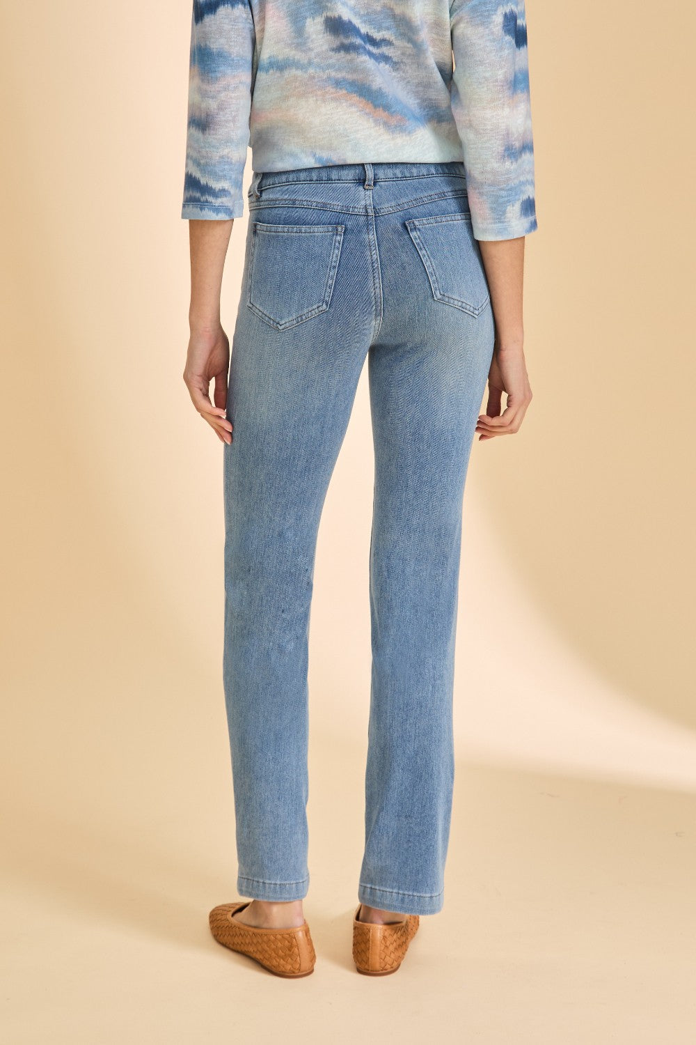 Person wearing a patterned top with light blue denim straight leg jeans