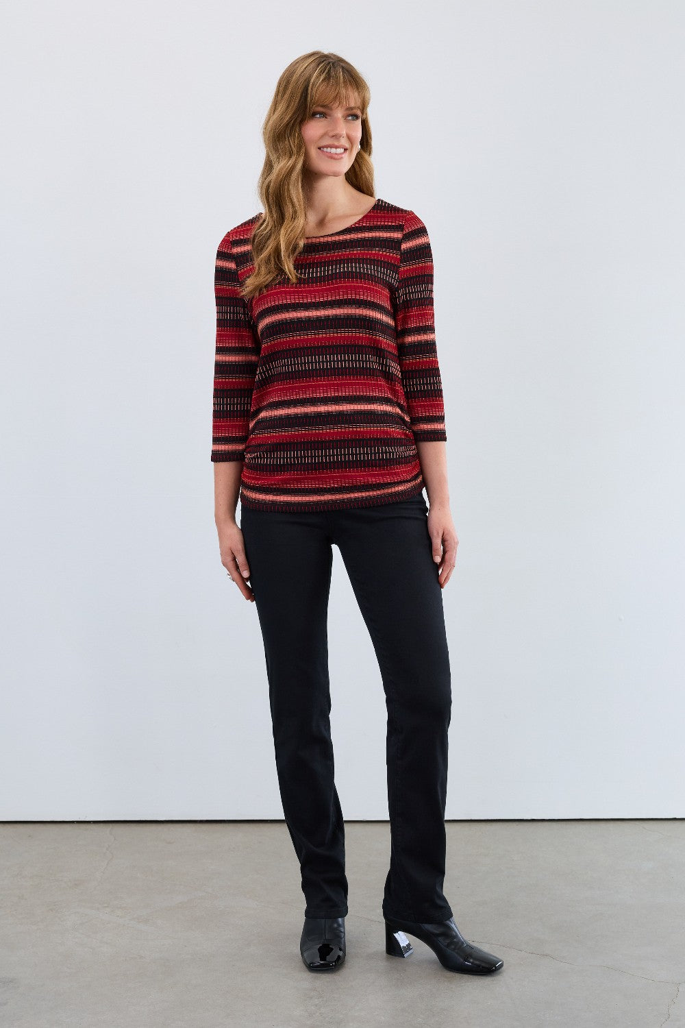 Woman wearing a red and black striped top with black pants against a white background