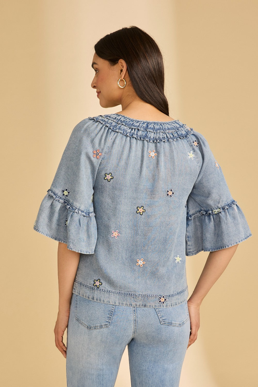 Woman wearing a light blue denim top with floral embroidery on a beige background