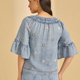 Woman wearing a light blue denim top with floral embroidery on a beige background
