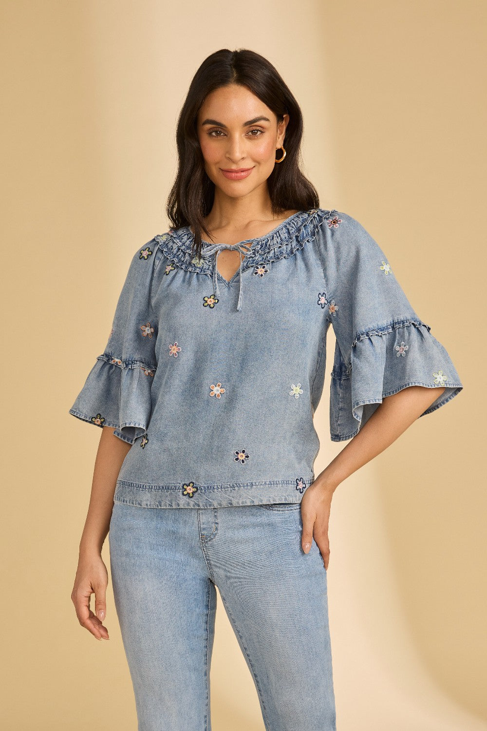 Woman wearing a blue denim blouse with floral embroidery on a beige background