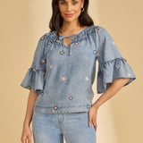 Woman wearing a blue denim blouse with floral embroidery on a beige background