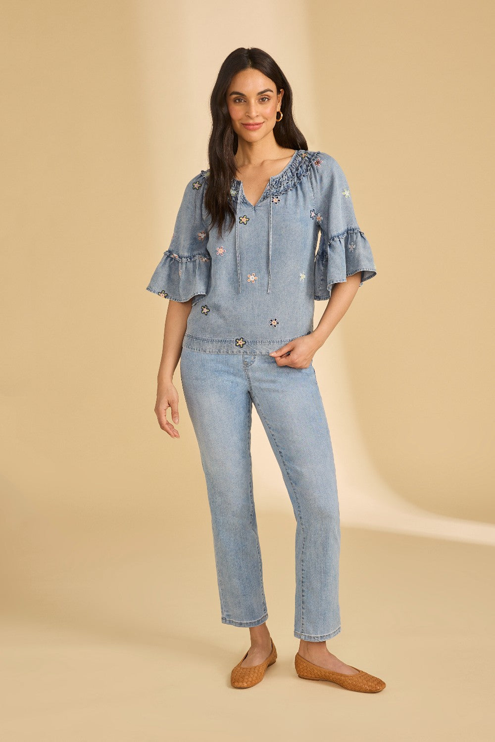 Woman wearing a blue denim outfit with ruffled sleeves on a beige background