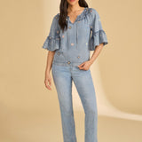 Woman wearing a blue denim outfit with ruffled sleeves on a beige background