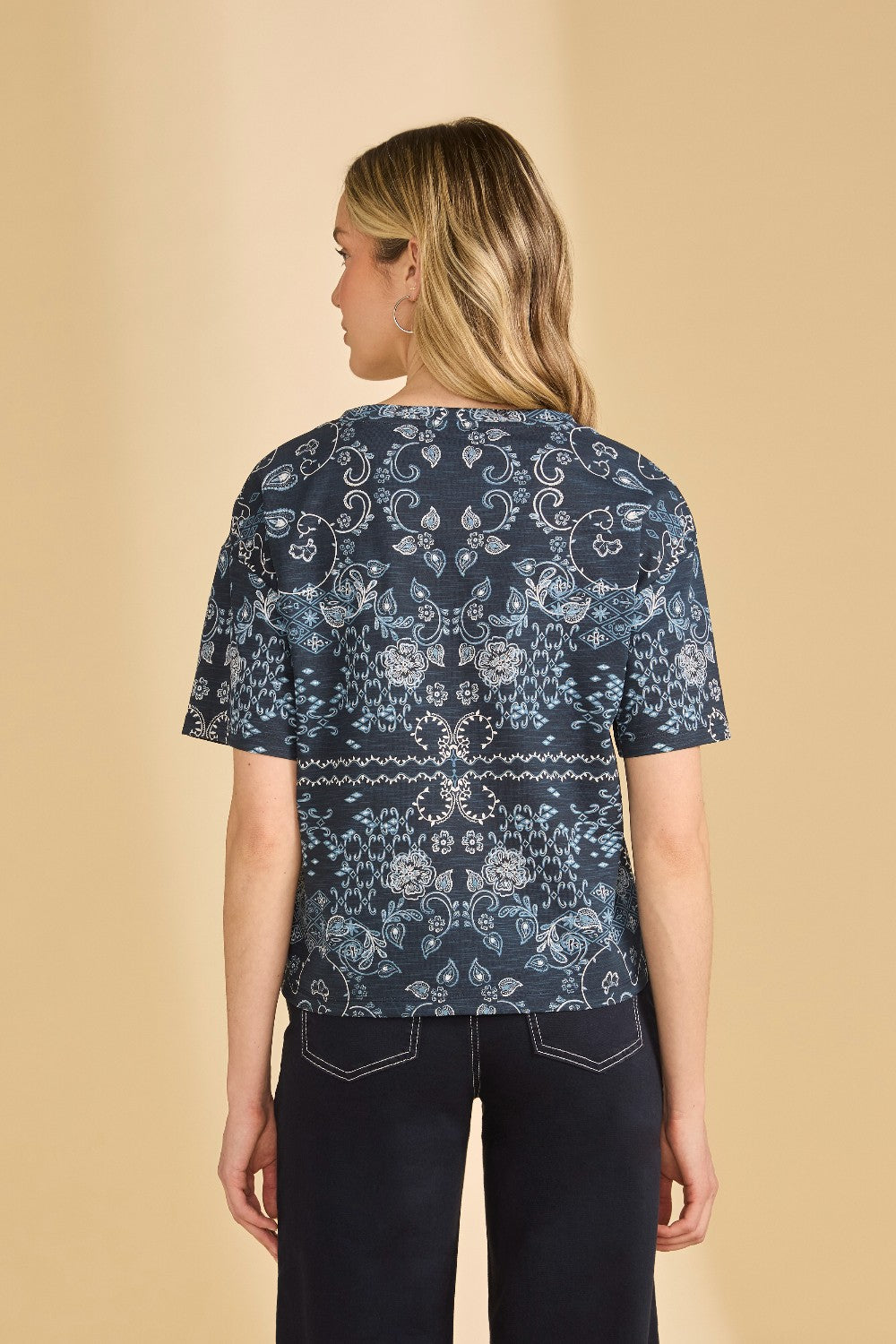 Woman wearing a blue patterned shirt and navy pants on a beige background