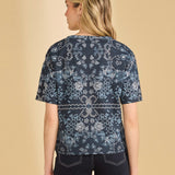 Woman wearing a blue patterned shirt and navy pants on a beige background