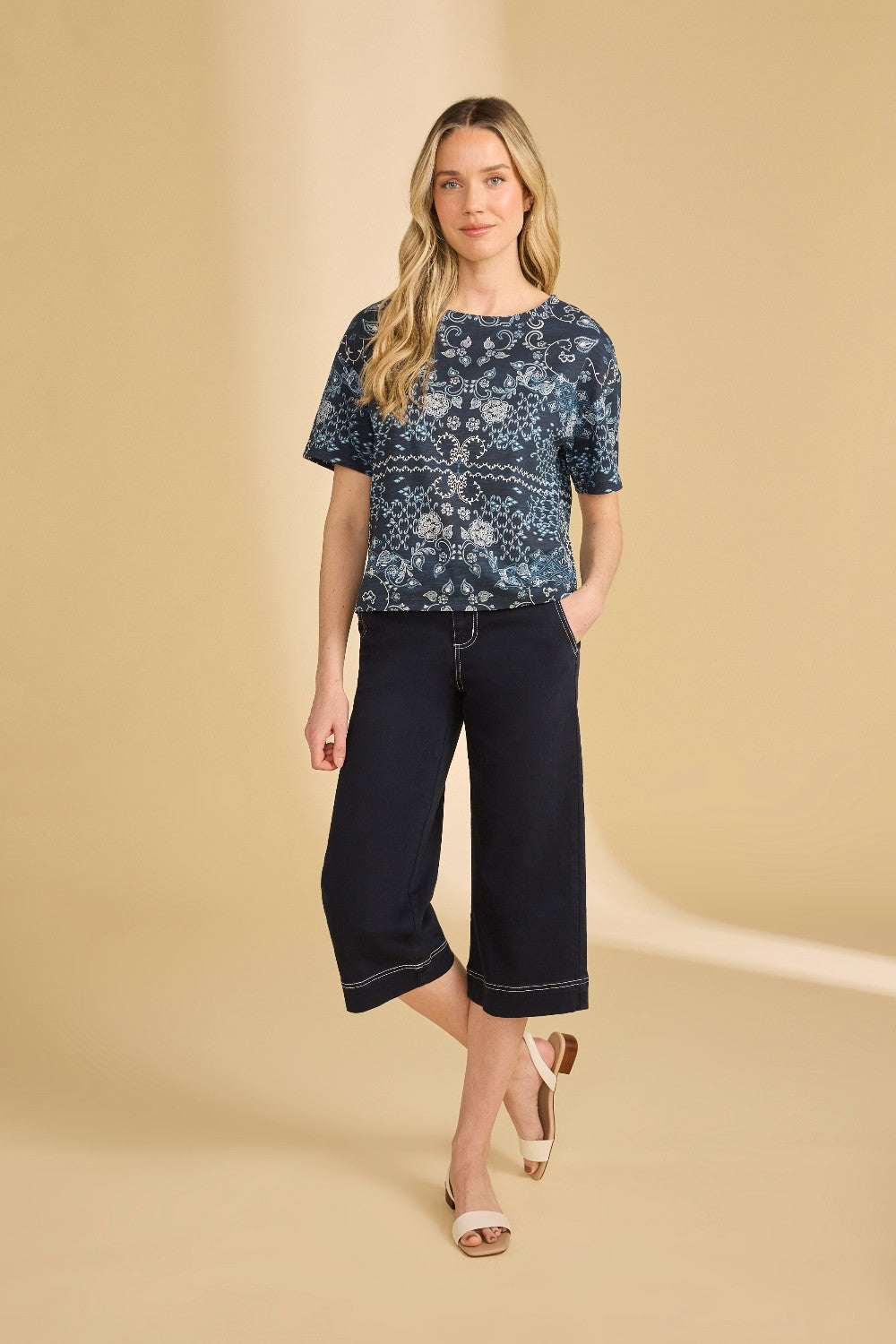 Woman wearing a patterned top and navy capri pants on a beige background