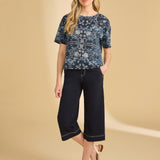 Woman wearing a patterned top and navy capri pants on a beige background