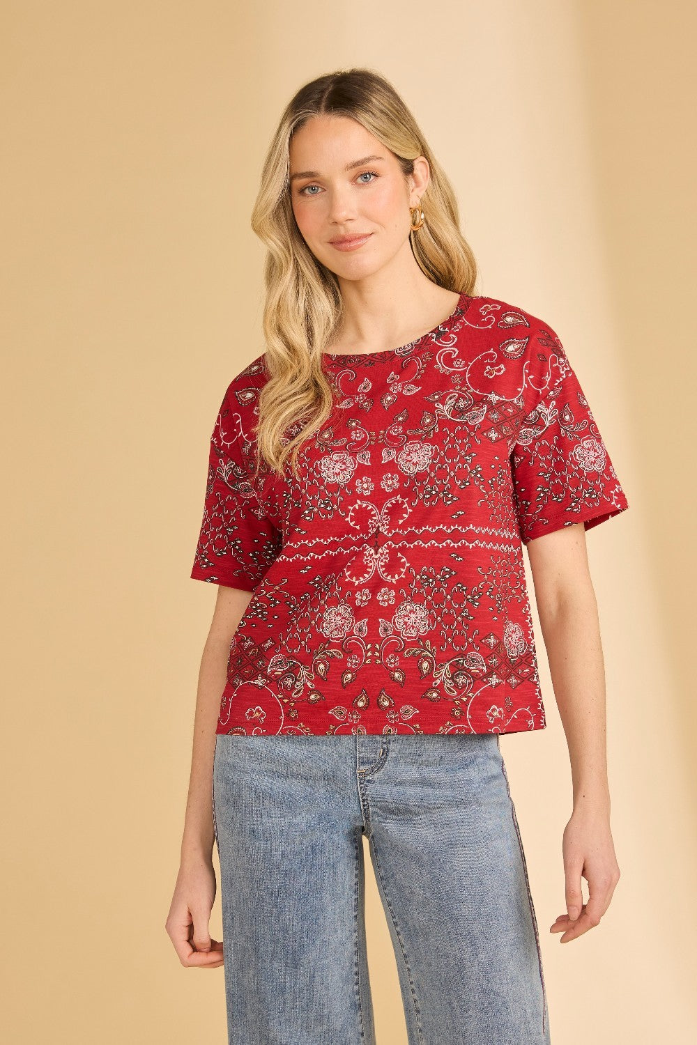 Woman wearing a red patterned top and blue jeans on a beige background