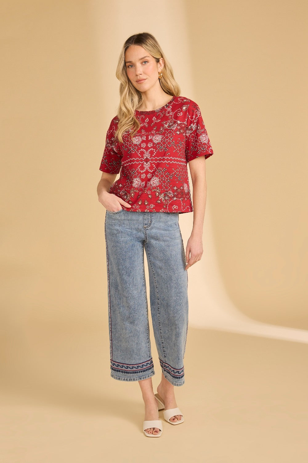 Woman wearing a red patterned top and blue jeans on a beige background