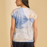 Woman wearing a light-colored top with blue patterns and dark shorts on a beige background