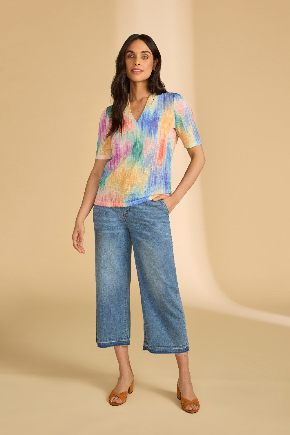 Woman wearing a colorful shirt and blue jeans on a beige background