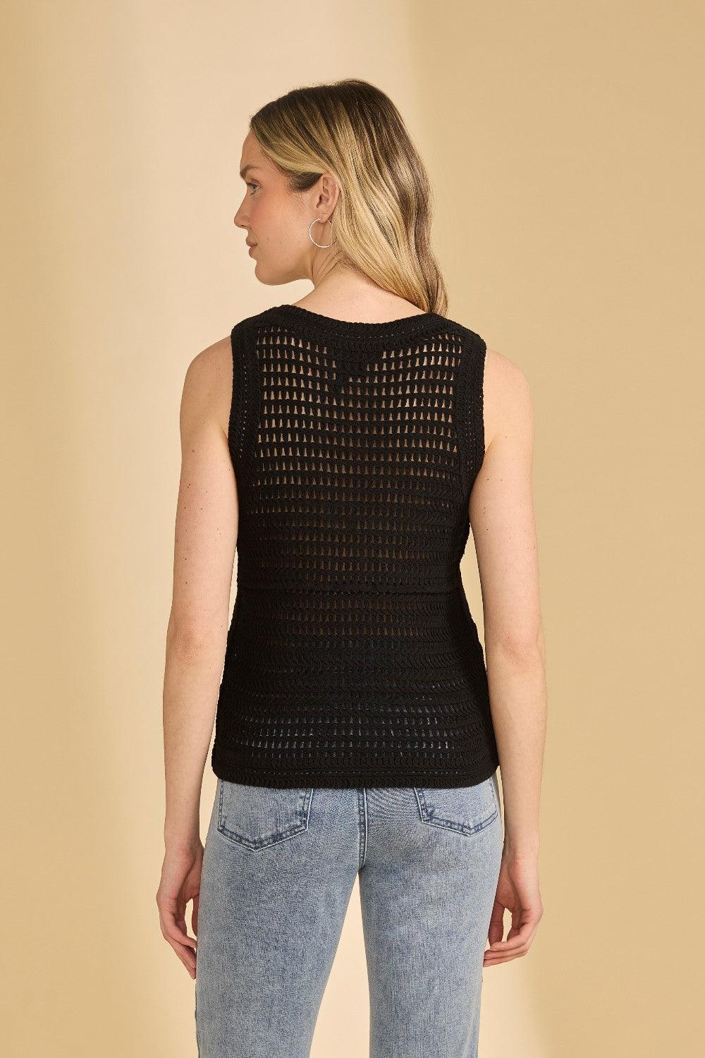 Woman wearing a black sleeveless top with a unique back design on a beige background