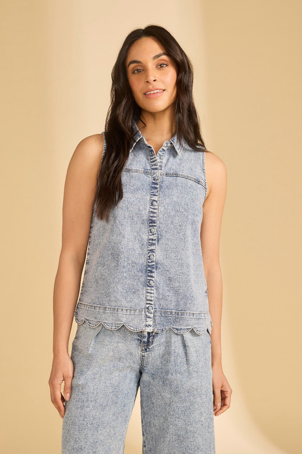 Woman wearing a sleeveless denim top and pants on a beige background