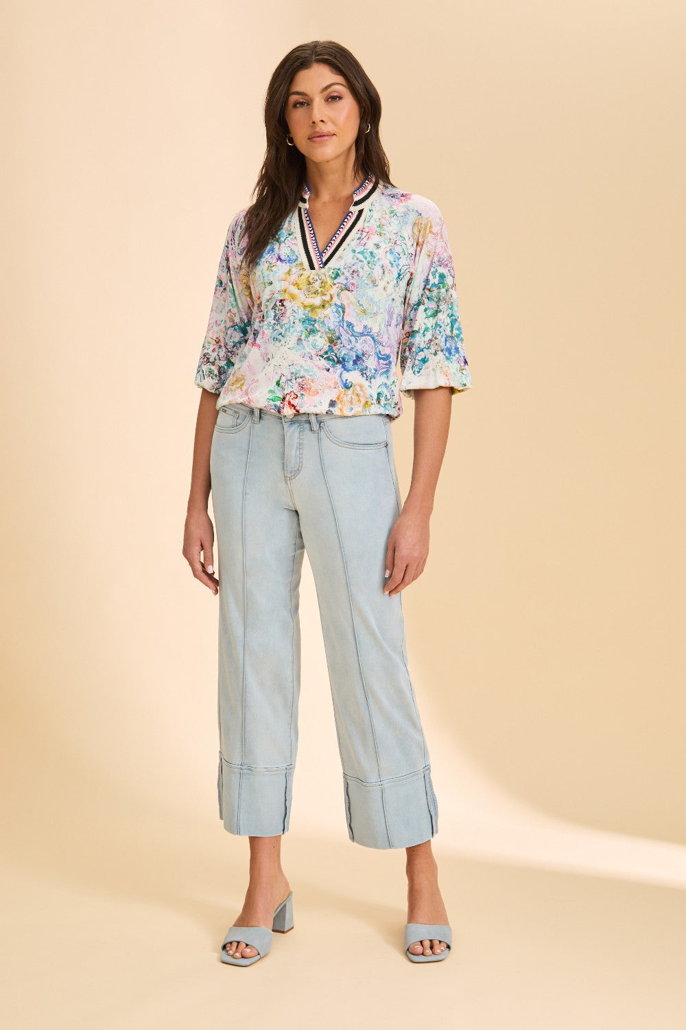 Woman wearing a floral blouse and light blue pants on a beige background