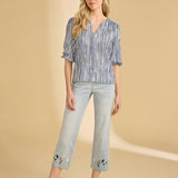 Woman wearing a striped blouse and light blue jeans with floral embroidery on a beige background