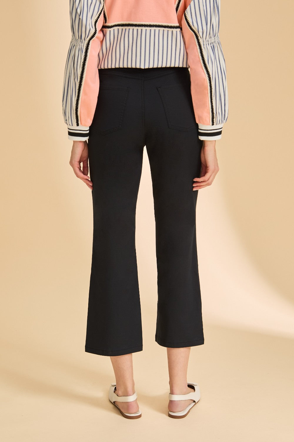Person wearing black pants and a striped top on a beige background