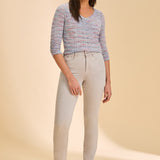 Person wearing grey jeans with a multi coloured shirt against a beige background