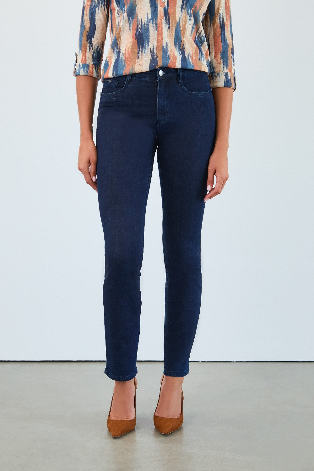 Person wearing blue jeans and a patterned top on a plain background