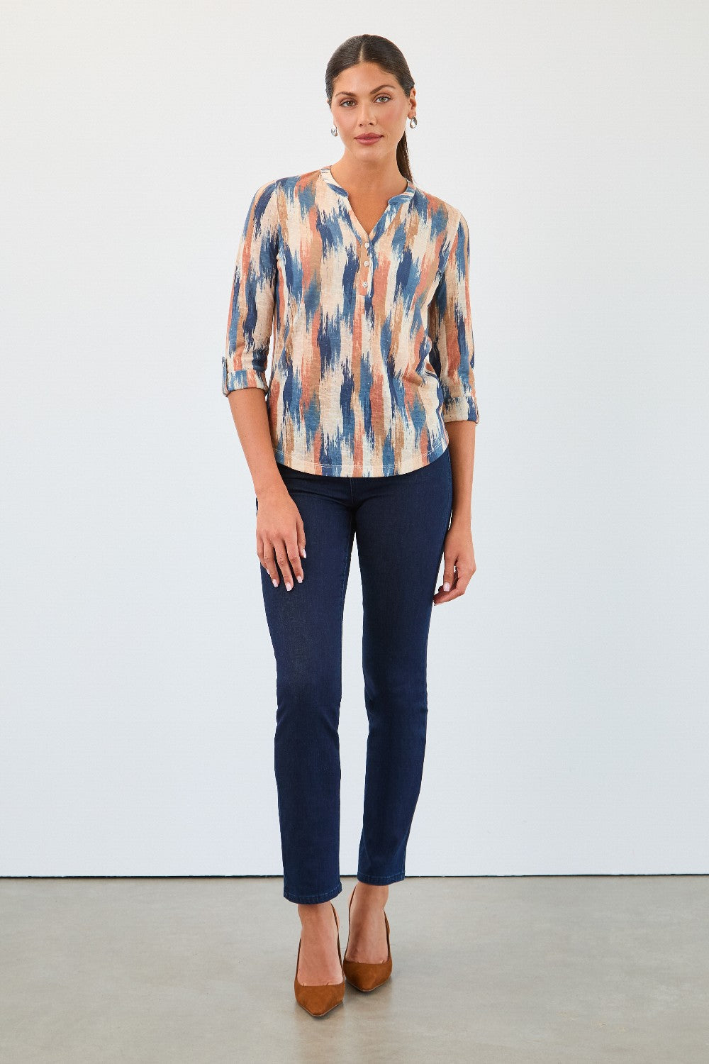 Woman wearing a patterned blouse and blue jeans against a white background