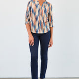 Woman wearing a patterned blouse and blue jeans against a white background