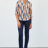 Woman wearing a patterned blouse and blue jeans against a white background