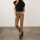 Woman wearing a short sleeve black top with dark tan jeans and black boots on a neutral background.