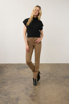 Woman wearing a short sleeve black top with dark tan jeans and black boots on a neutral background.